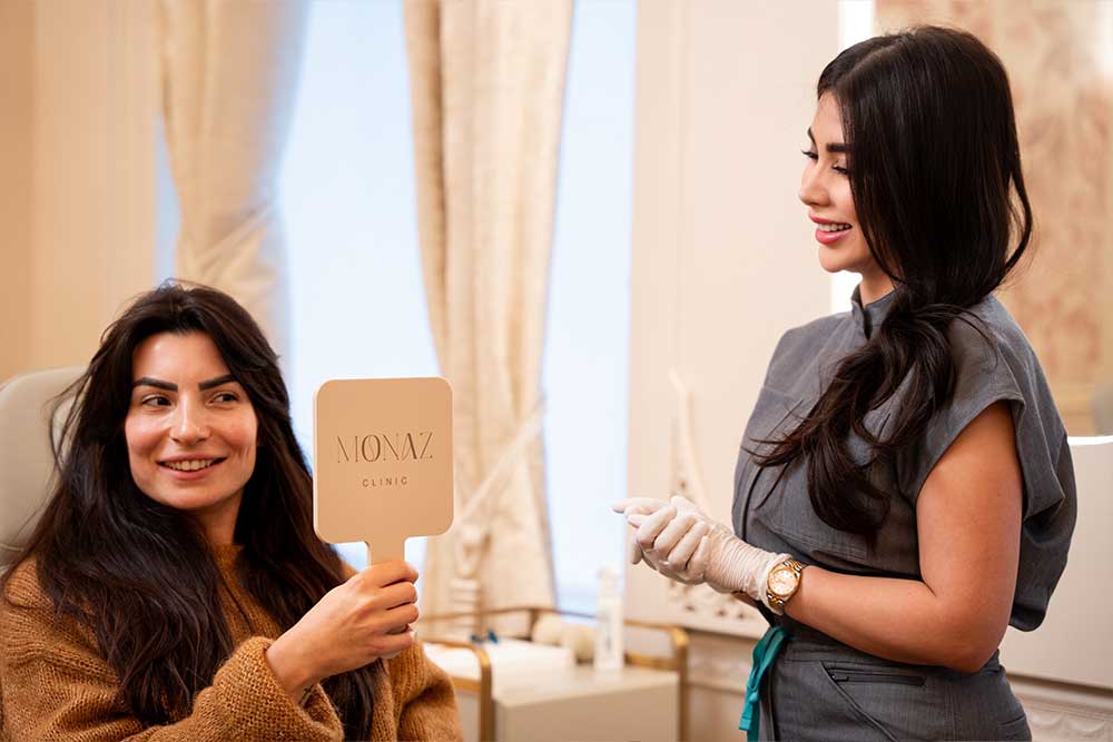 Mona Zirak, founder of Monaz Clinic, reviewing aesthetic results with a patient using a clinic mirror during consultation.